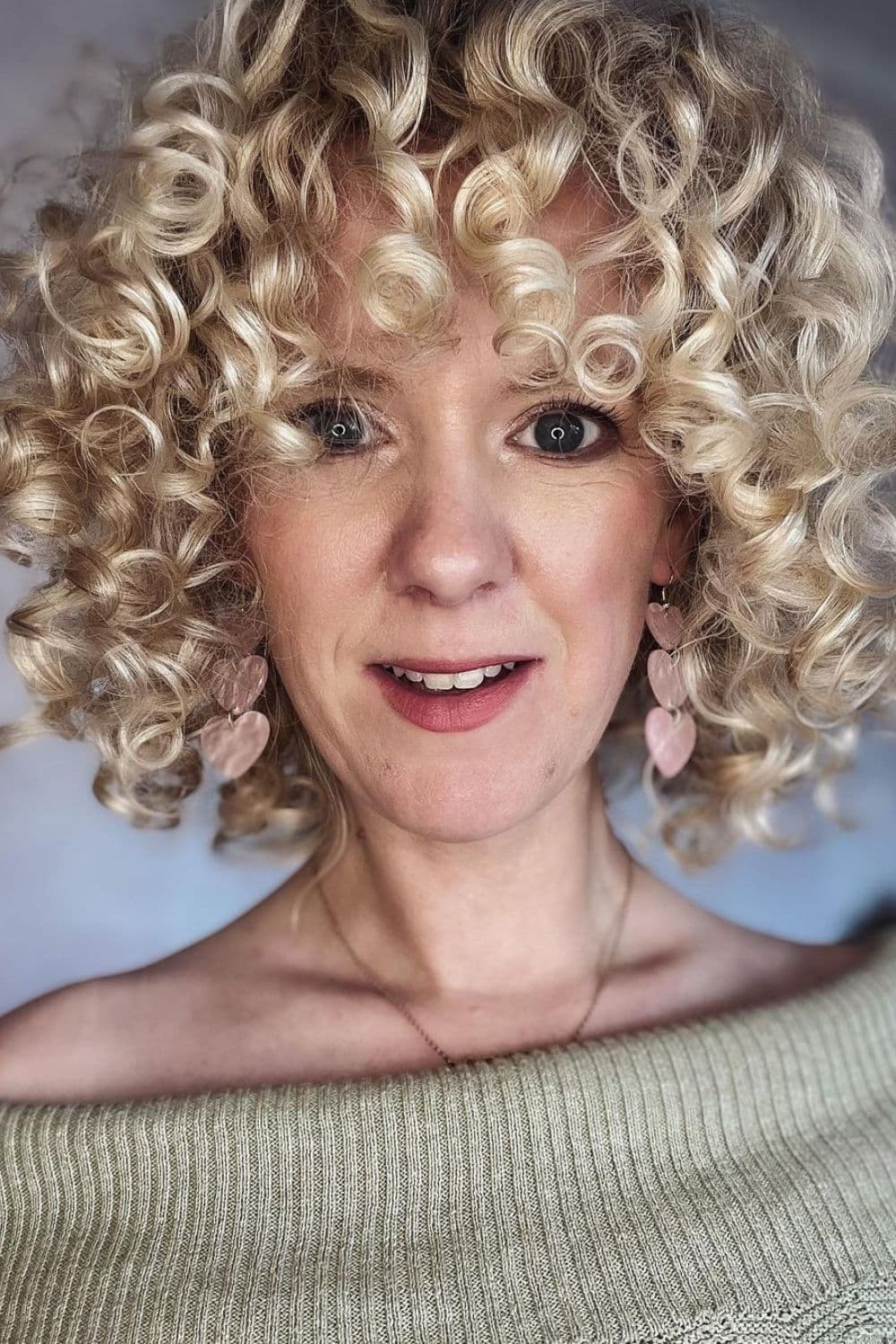 A woman with blonde deva cut with curly bangs.