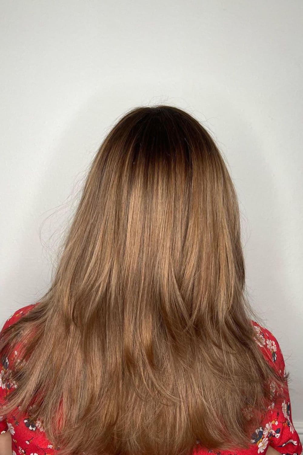 A woman with long layered dirty blonde hair with shadow root.