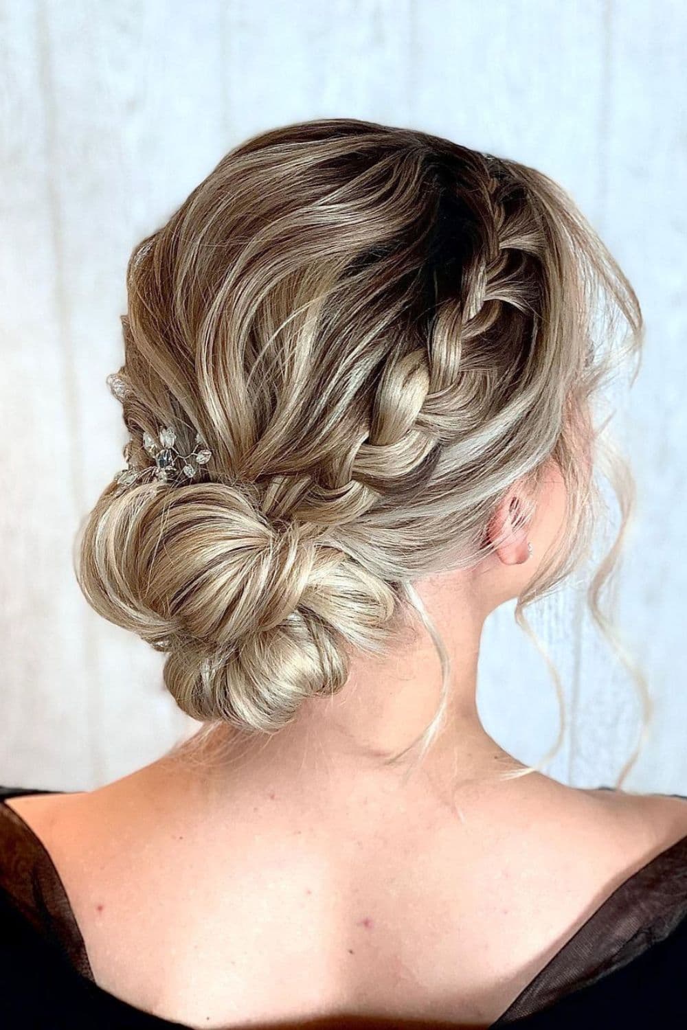 A woman with a blonde French braid bun with shadow roots.