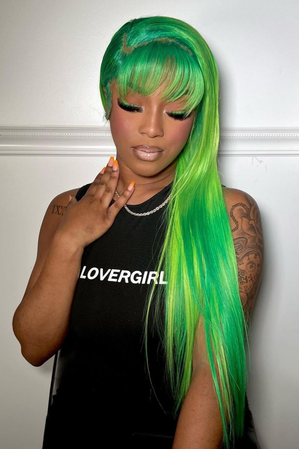 A woman with a green ombre quick weave with bangs.