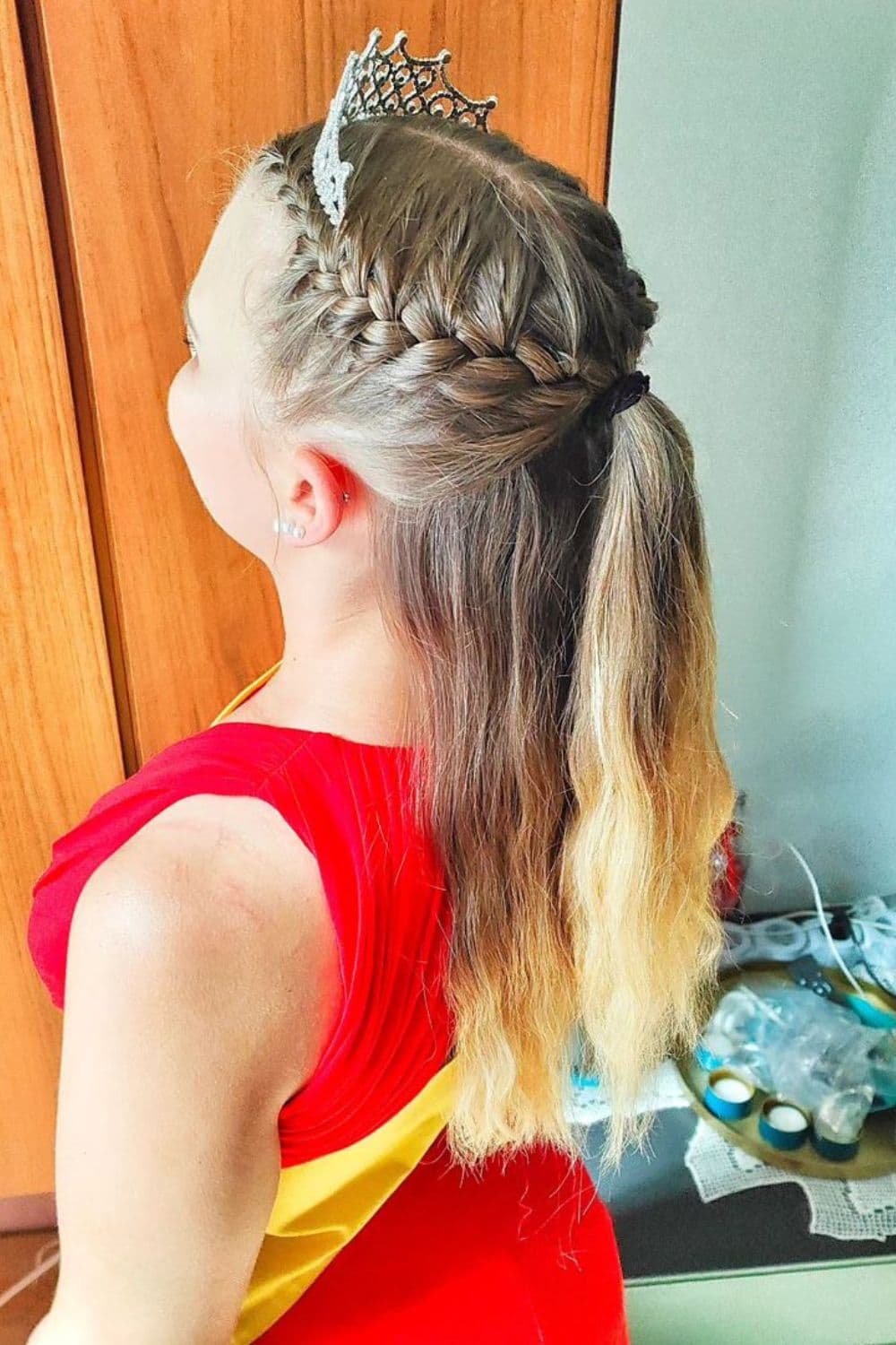 A girl wearing a princess crown with a blonde half French braid.
