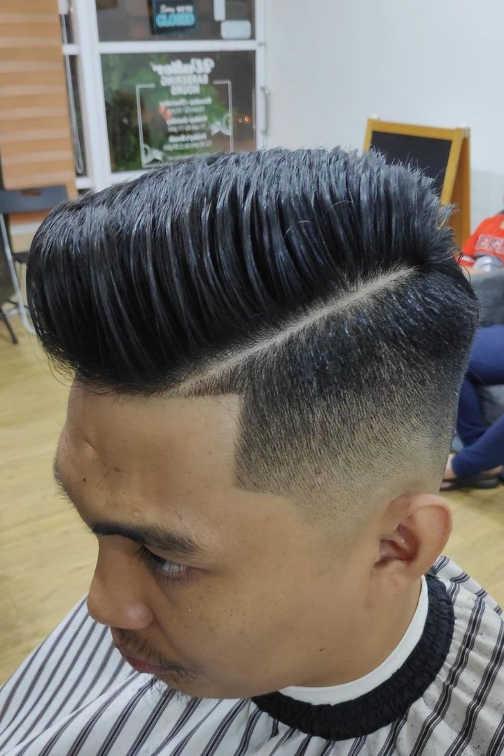 A man with a black hard side part cut.