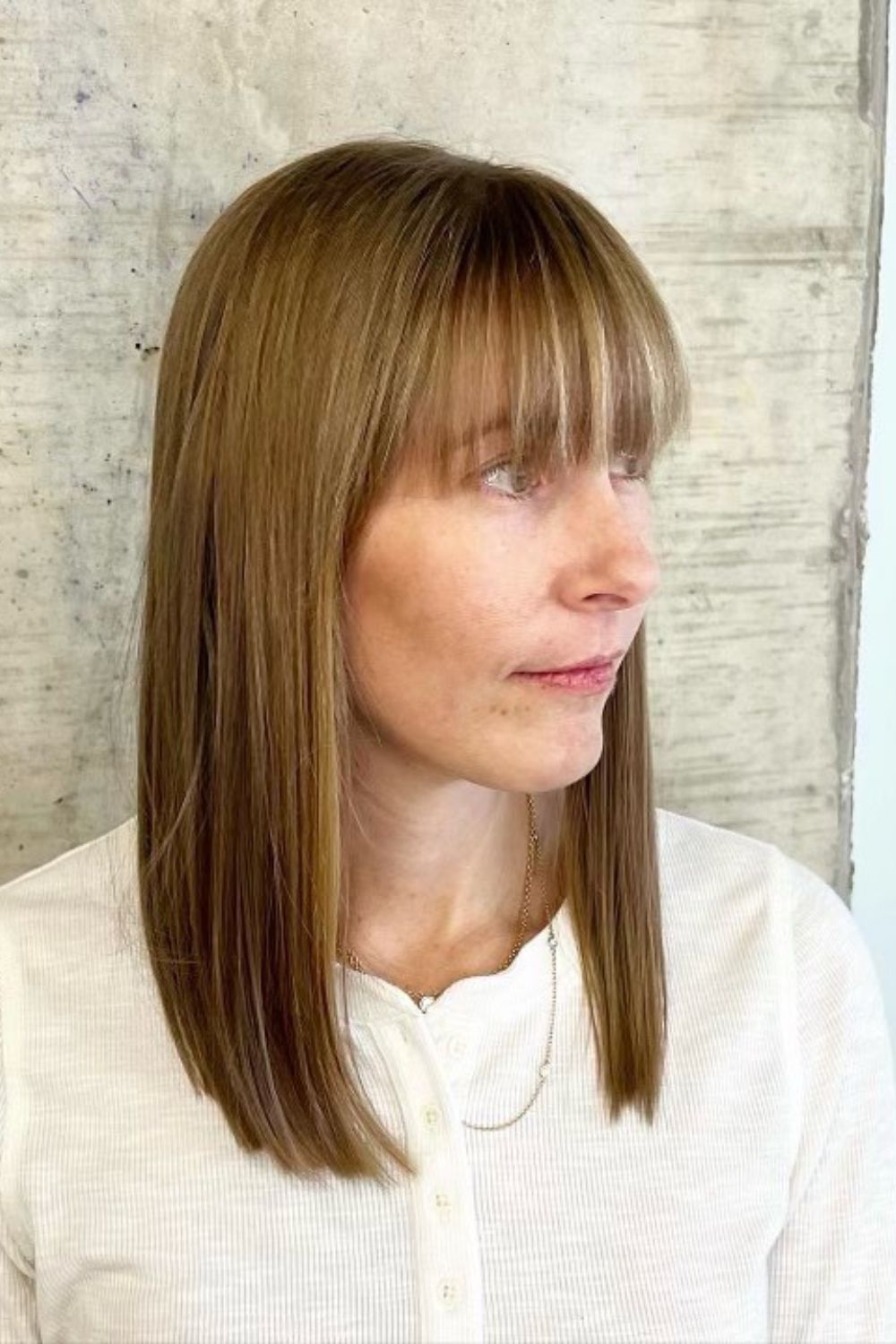 A woman with long blonde blunt cut with full bangs.