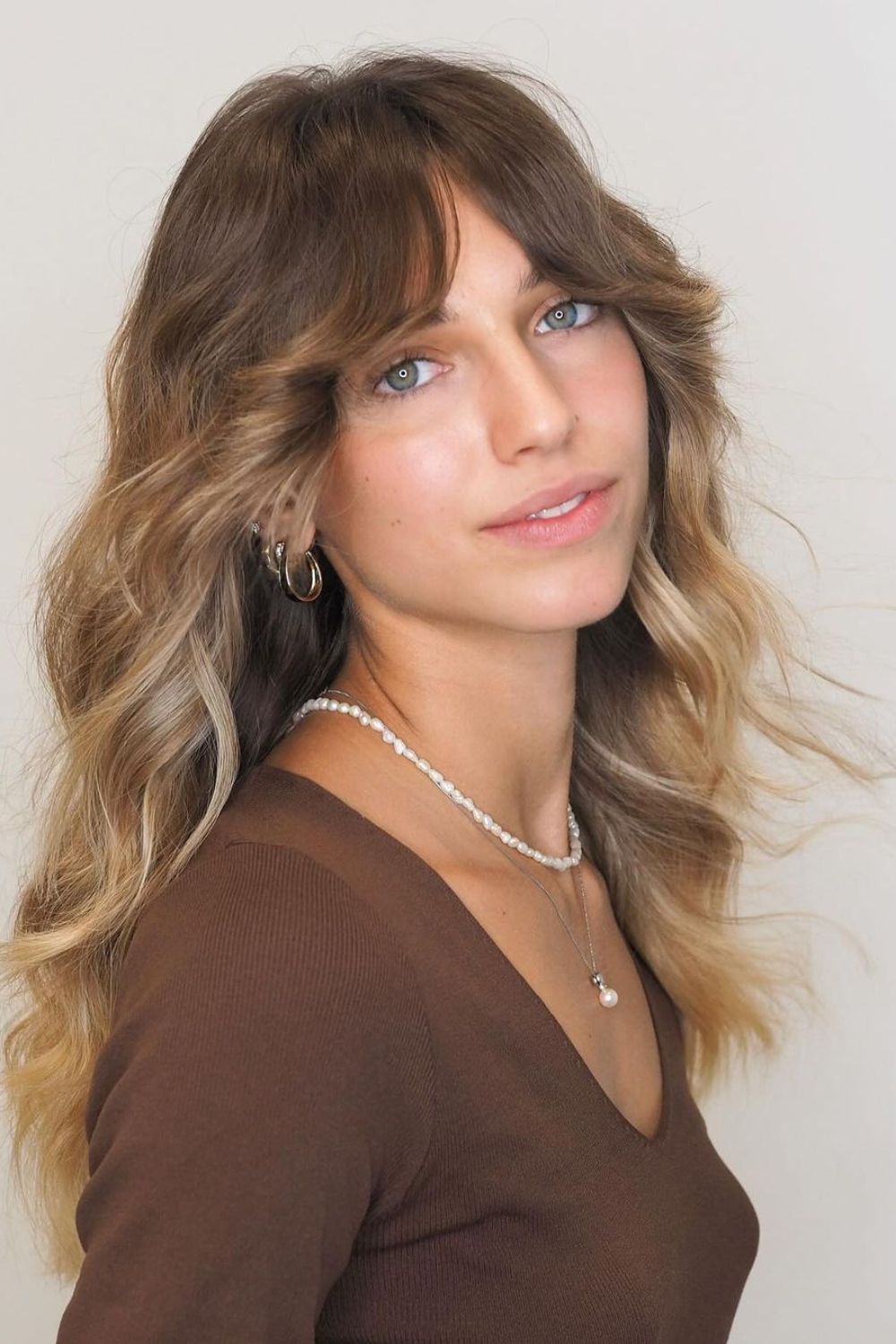 A woman with long bronde layers and curtain bangs.