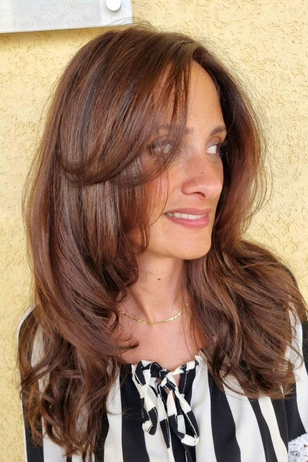 A woman with brown long waves with curtain bangs.