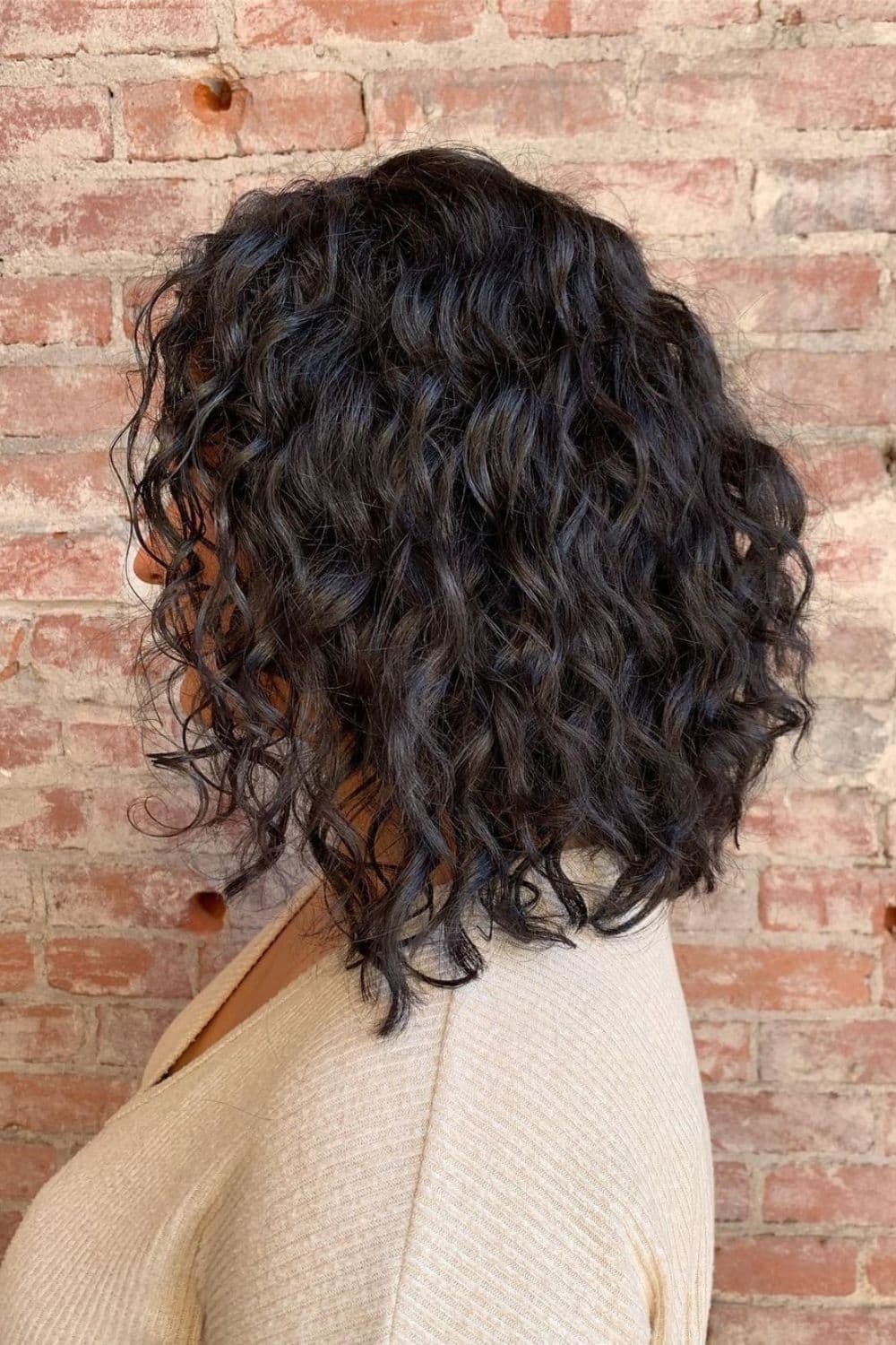 A woman with a black loosely curled inverse lob.