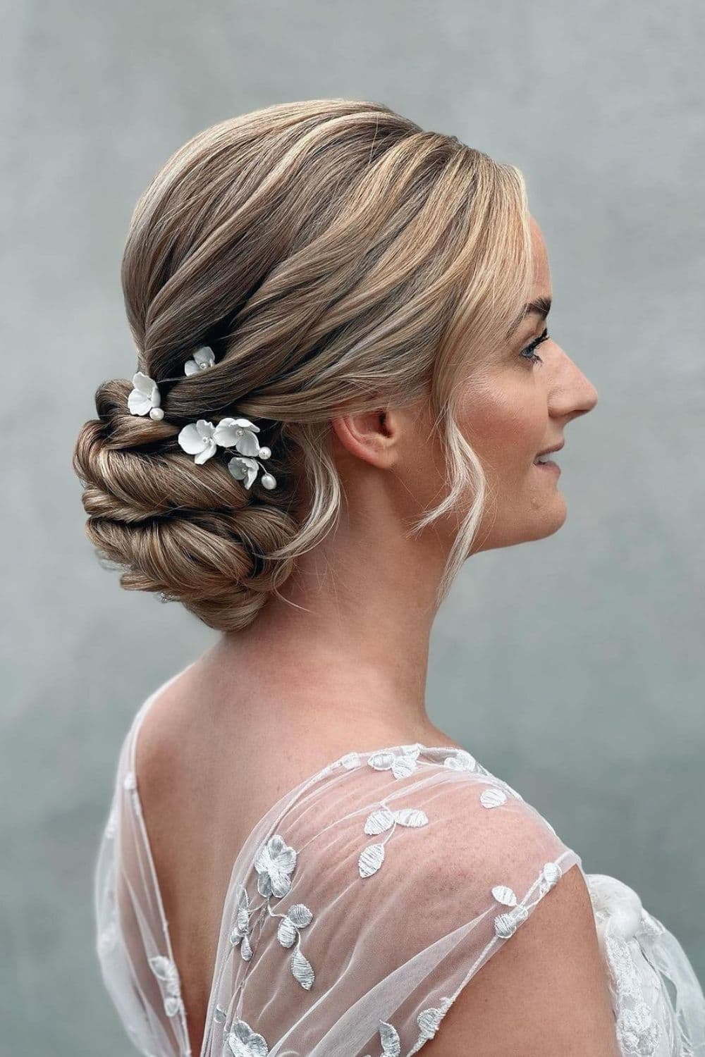 A woman with a blonde low bun and flower hair accessory.