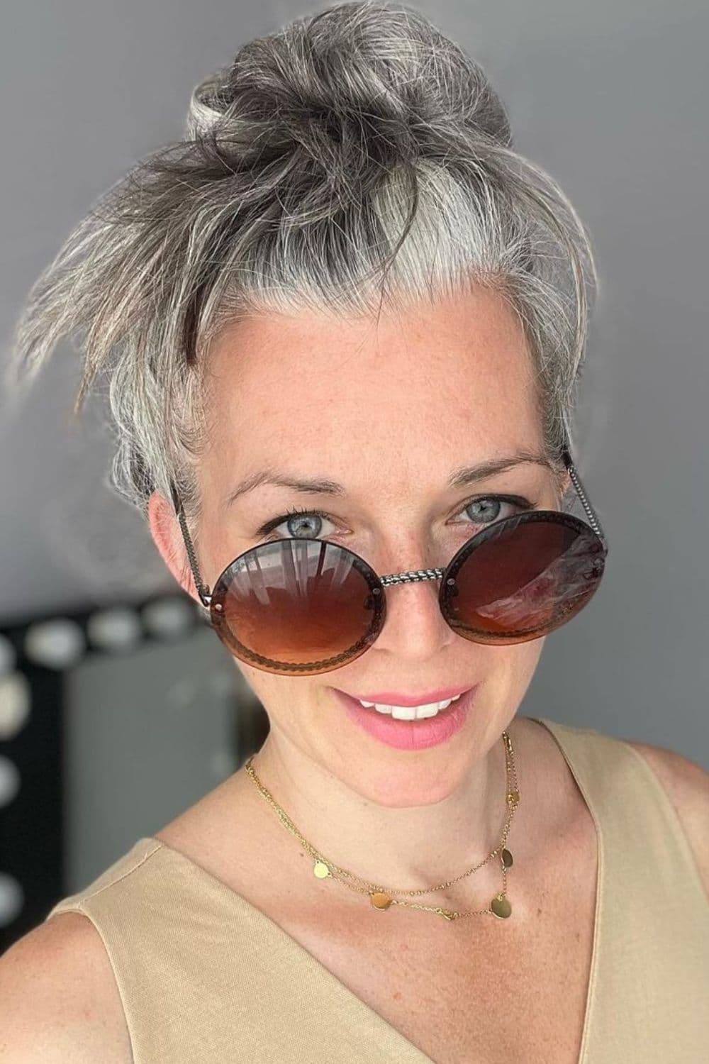 A woman wearing sunglasses with natural gray hair in a messy bun.