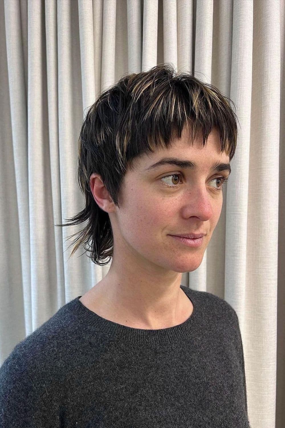 A woman with a black mixie cut with highlights.