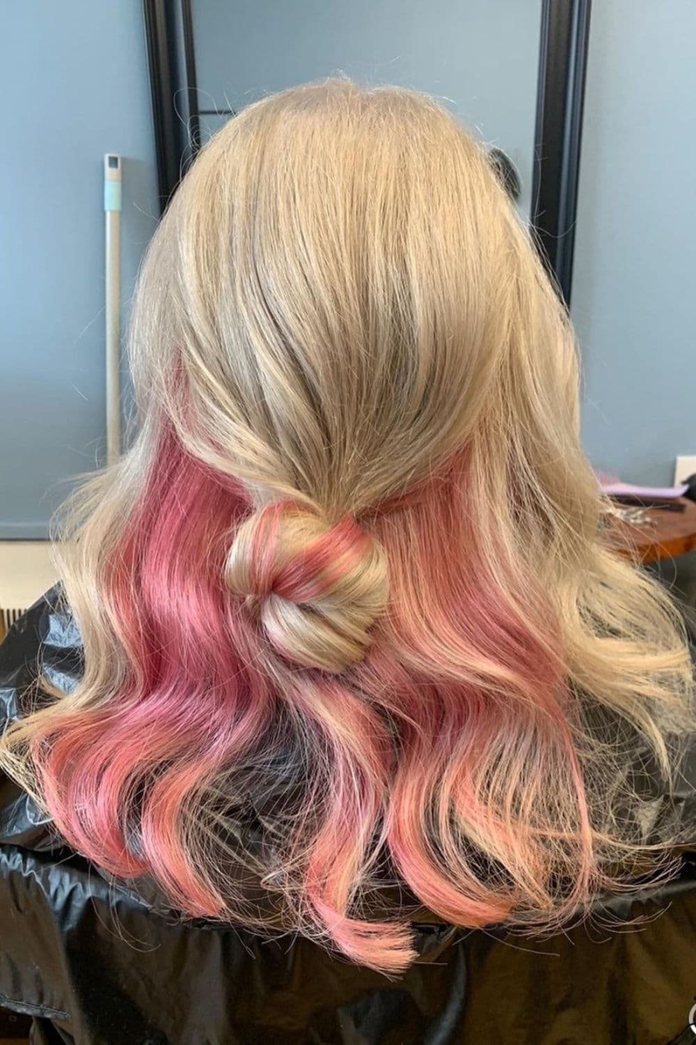 A woman with long blonde hair and pink peekaboo balayage.