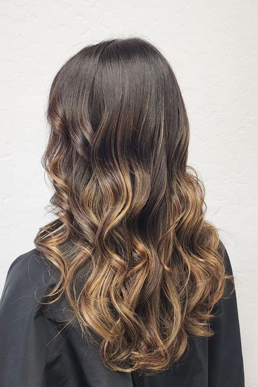 A woman with long rooted balayage with curls.