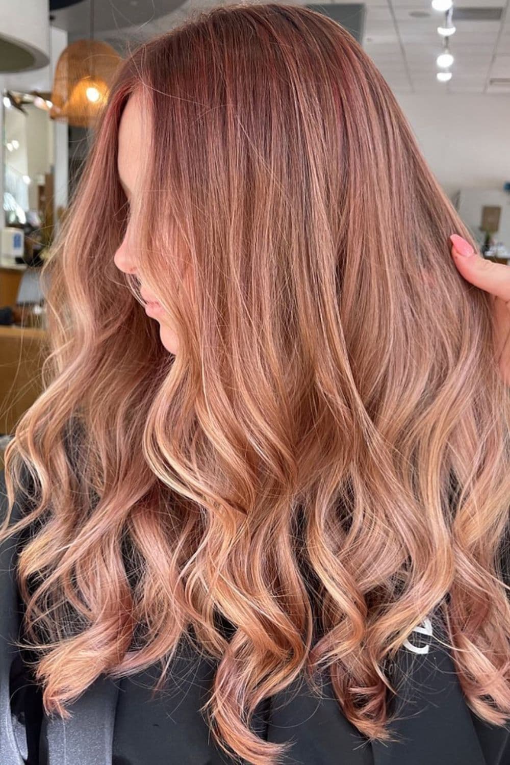 A woman with long rose gold balayage with curls.