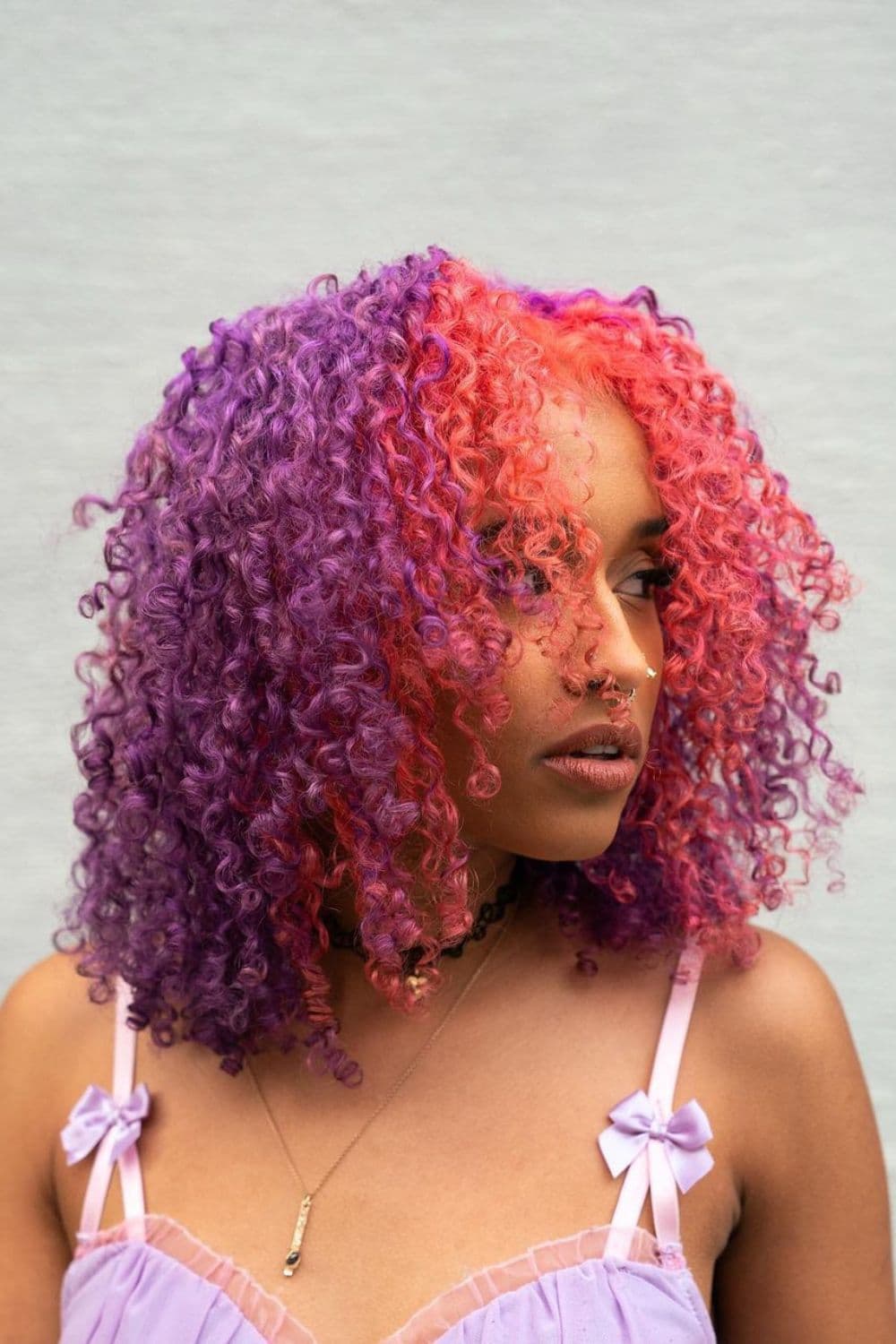 A woman with short curly hair with pink money pieces on lilac purple hair.