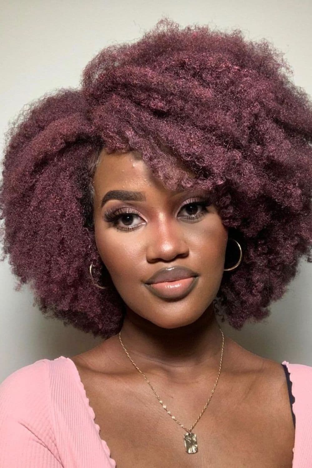 A woman with short pink side-parted natural 4C hair.