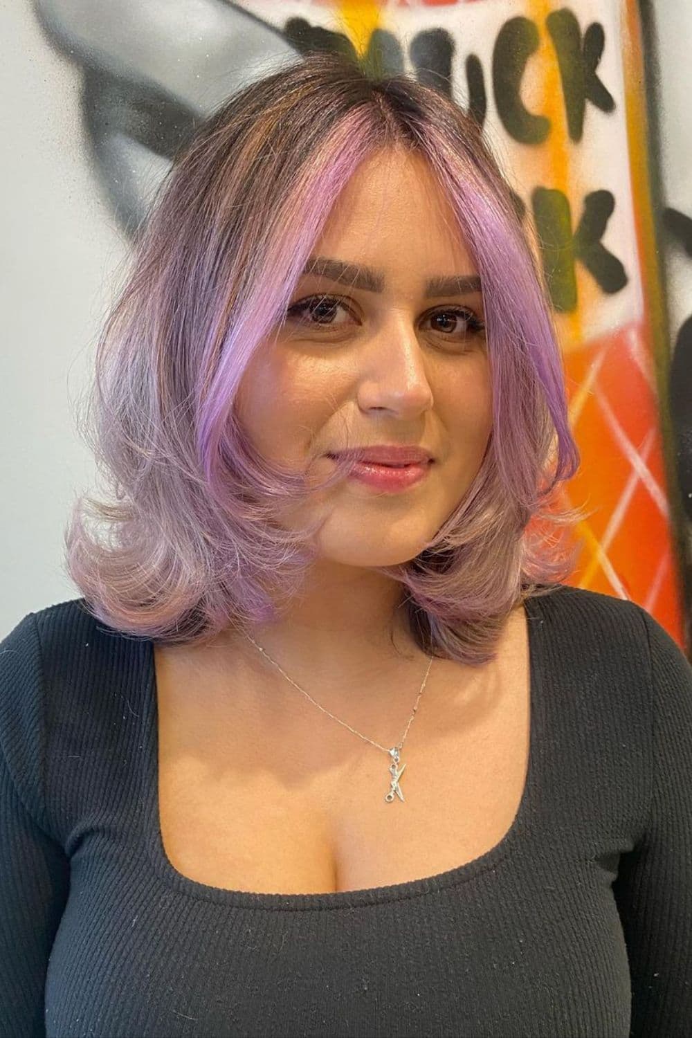 A woman with shoulder-length lavender hair with face-framing layers and money pieces.
