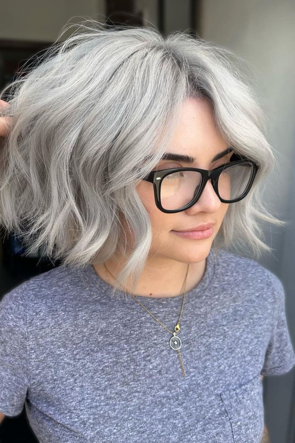 A woman wearing black eyeglasses with a silver blonde wavy bob cut.