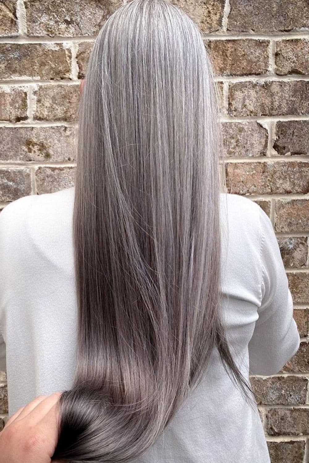A woman with long straight silver hair with lowlights.