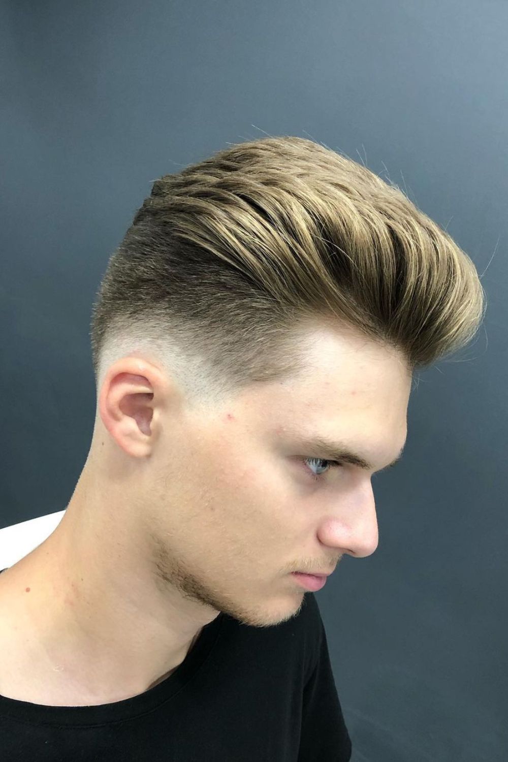 A man with a blonde slicked back mid-fade hair.