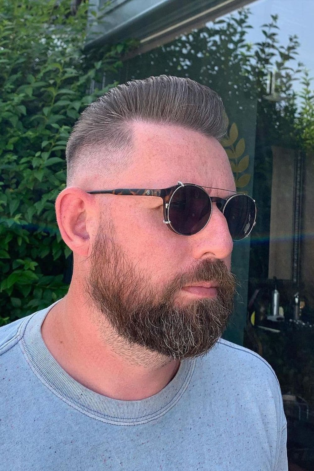 A man wearing round sunglasses with slicked back pompadour with skin fade.