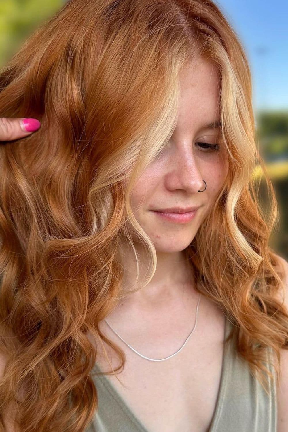 A woman with long wavy strawberry blonde with blonde money pieces.