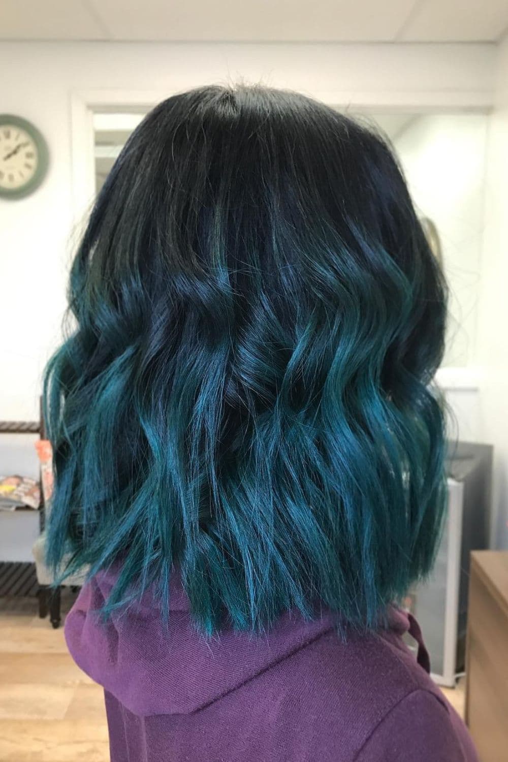A woman with teal-toned blue black long bob with beach waves.