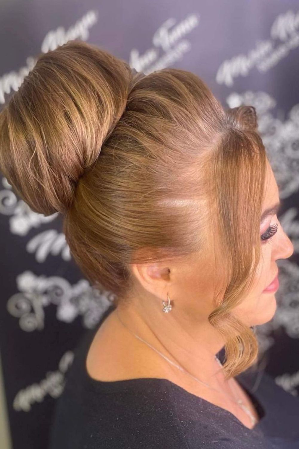 A woman with a blonde top knot chignon with face-framing pieces.