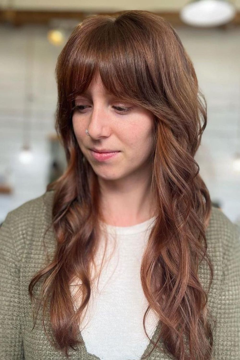 A woman with long brown wavy hair with closed curtain bangs.