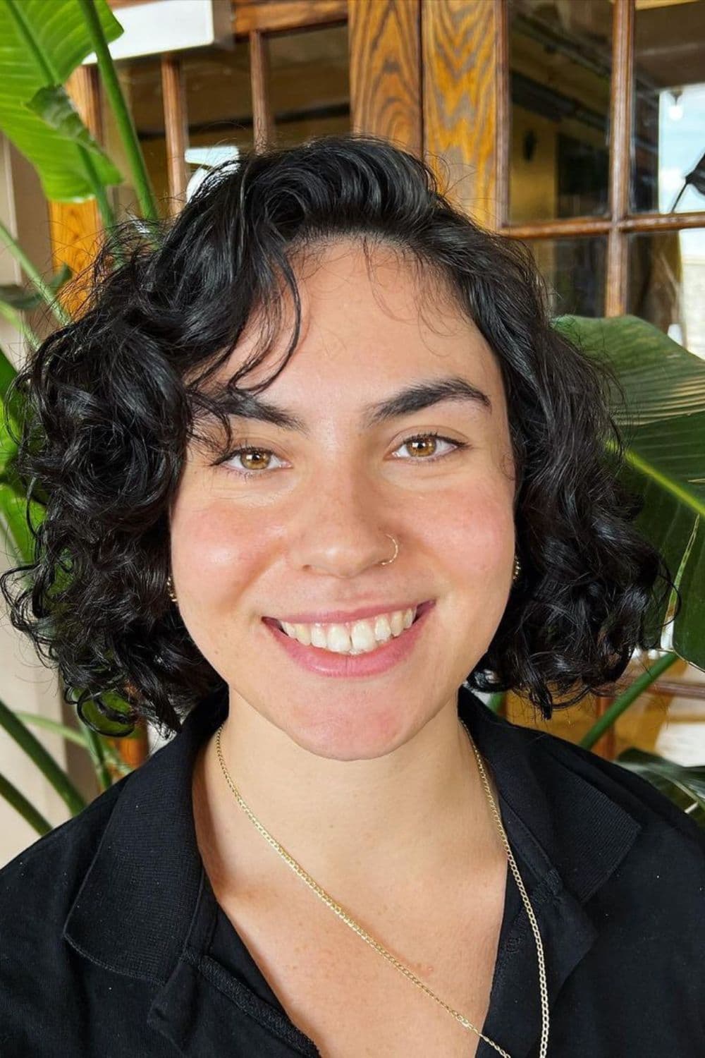 A woman with a black curly chin-length bob with a deep side part.