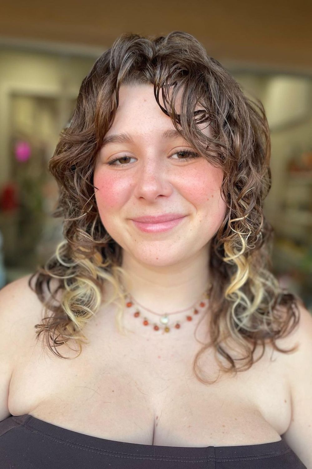 A woman with brown curly hair and curly curtain bangs.