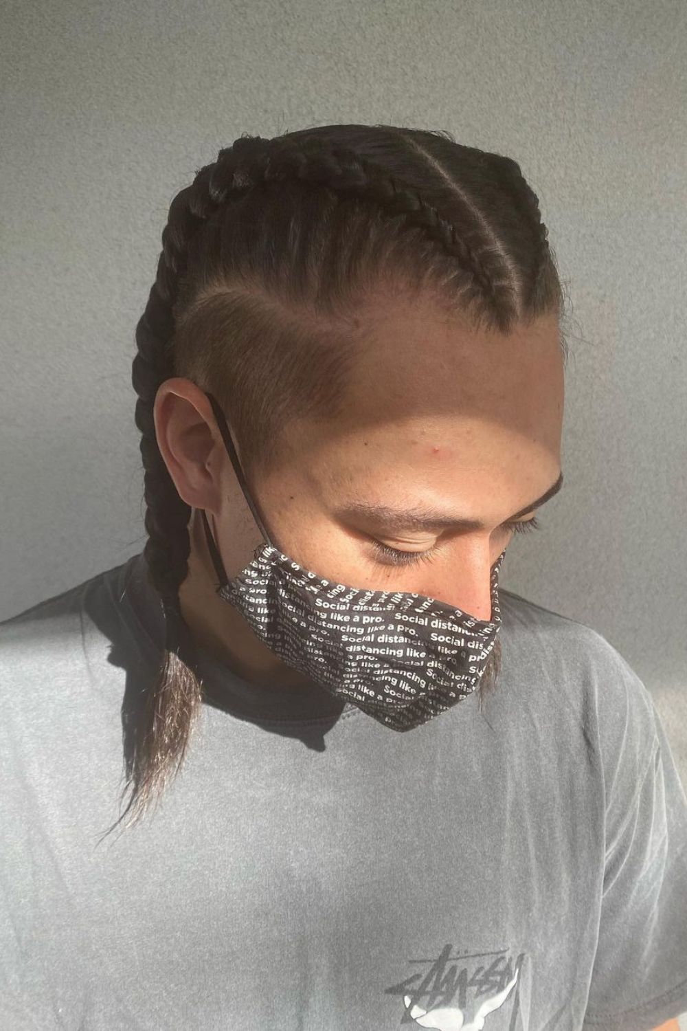 A man in faded double Dutch braids is wearing a face mask.