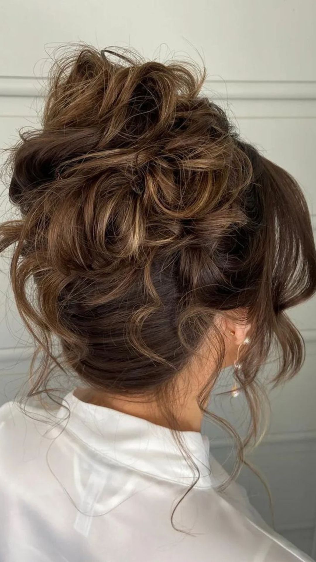 A woman with a textured high bun with loose curls.