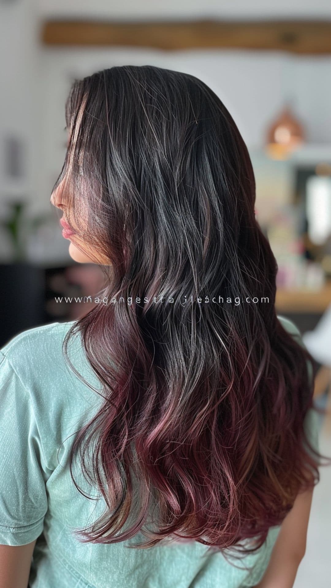 A woman modelling a long, layered cut with deep natural root and soft burgundy tips.