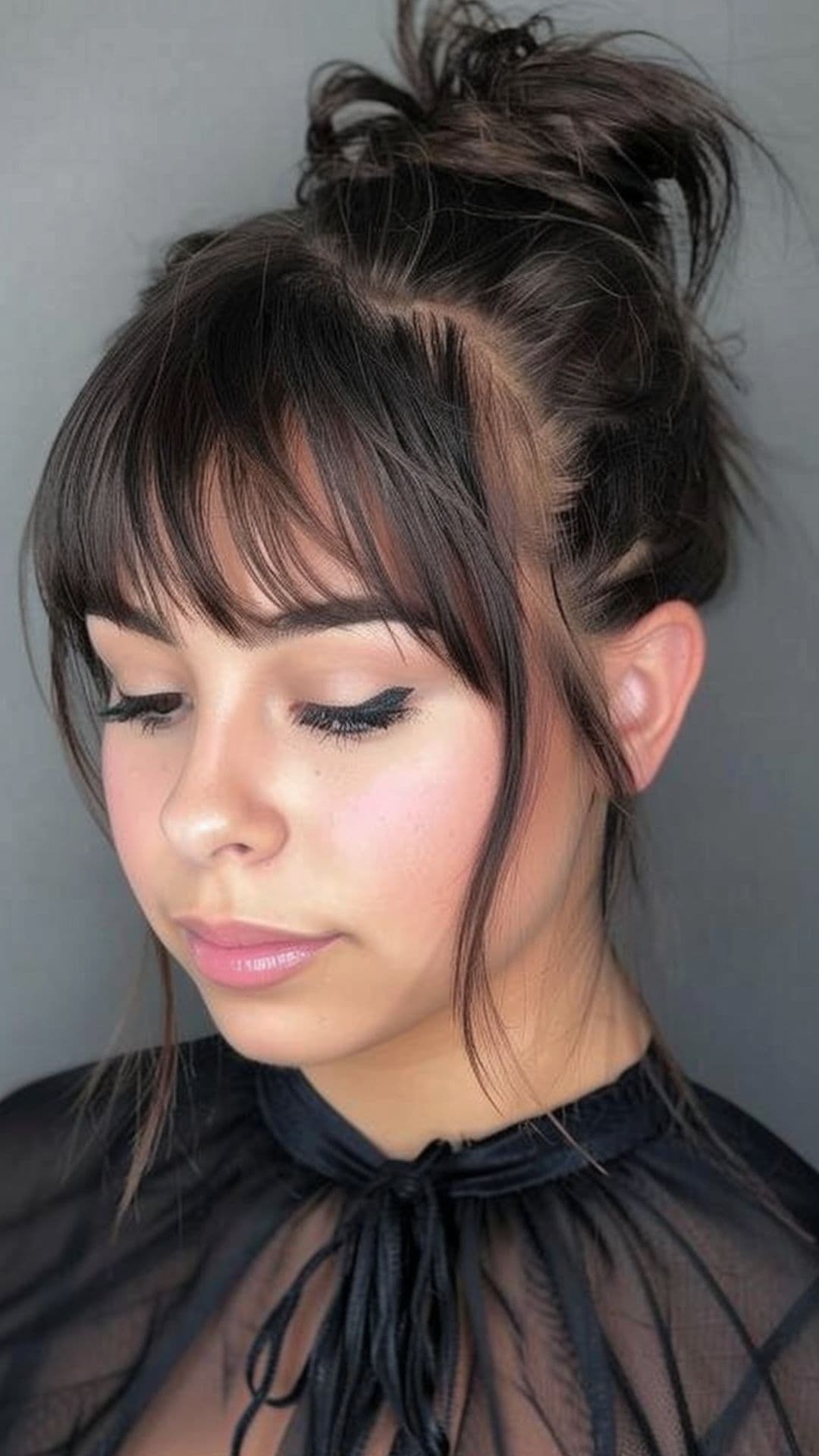 A round-faced woman modelling a messy bun with bangs.