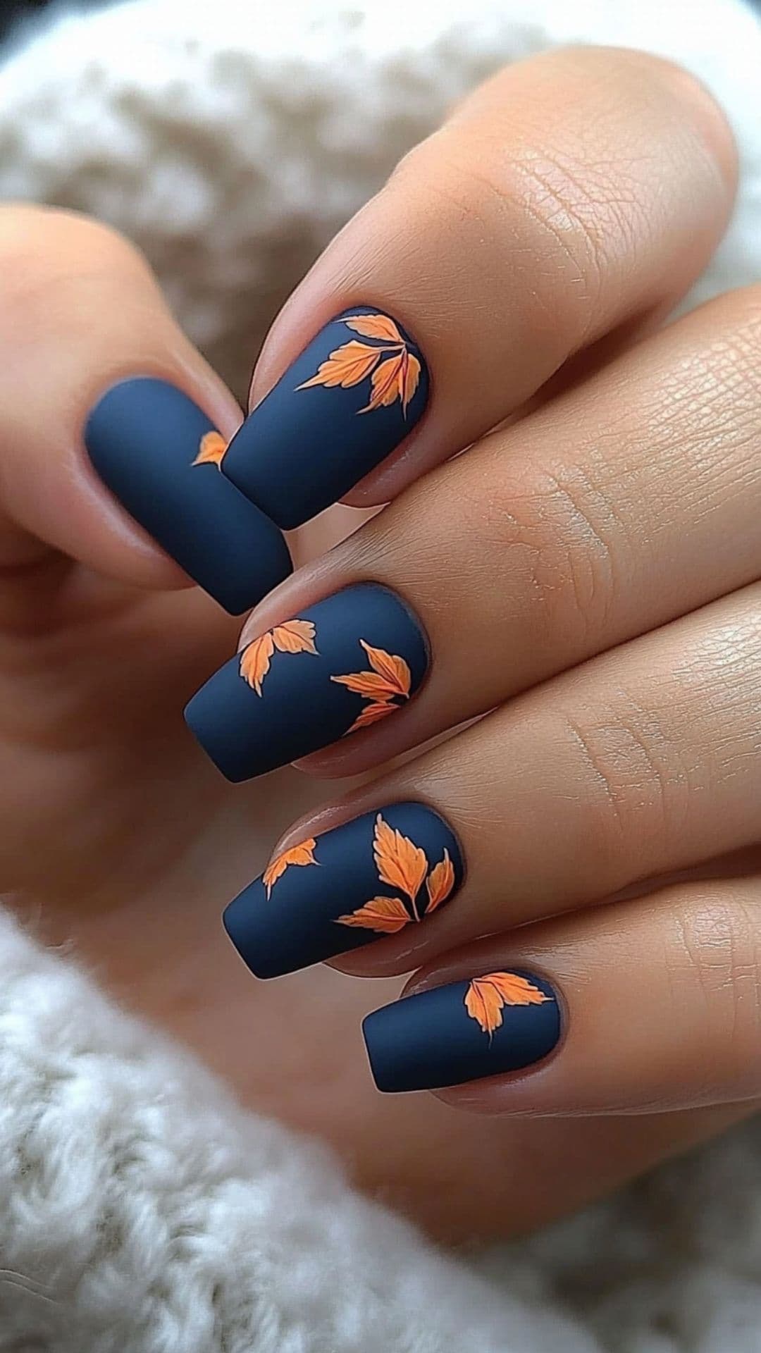 Woman's nails modelling Matte Blue with Orange Leaf Designs.