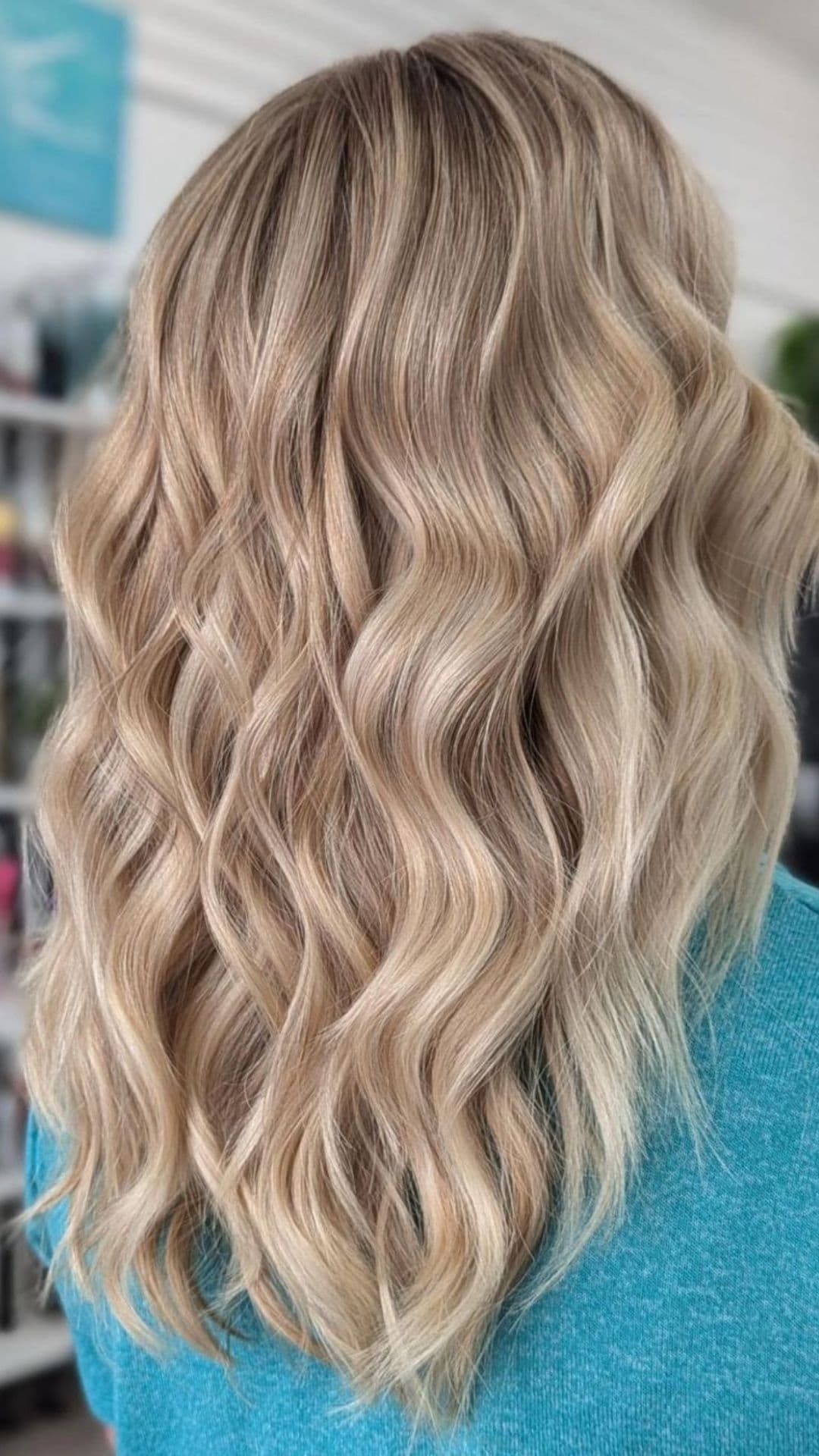 Back view of wavy Champagne Blonde hair worn by a person in a blue sweater.