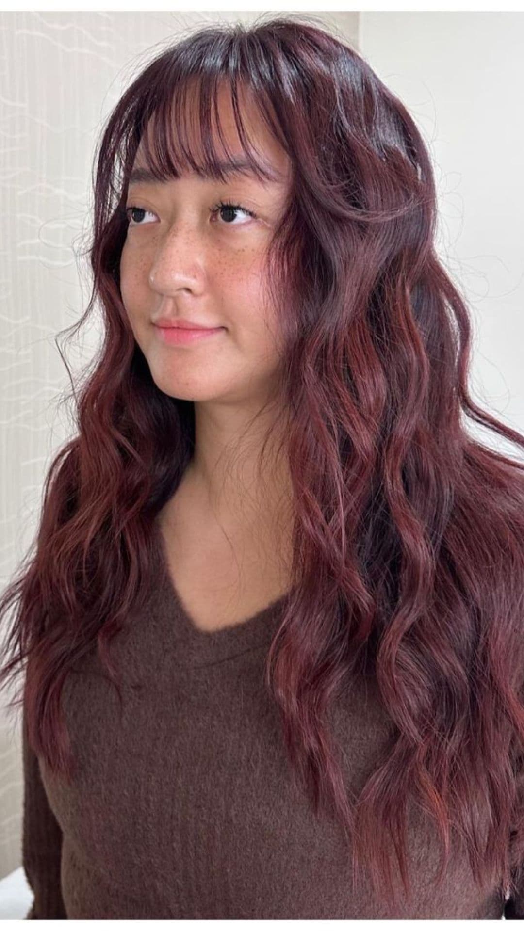 Woman with wavy, cranberry red hair, wearing a brown sweater, looking slightly to the side.