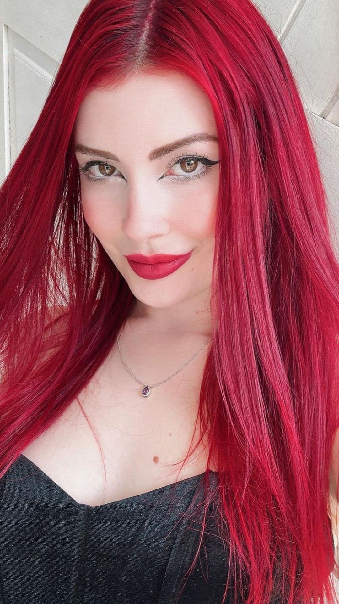 Person with long Holly Berry Red hair, wearing a black top and a necklace.