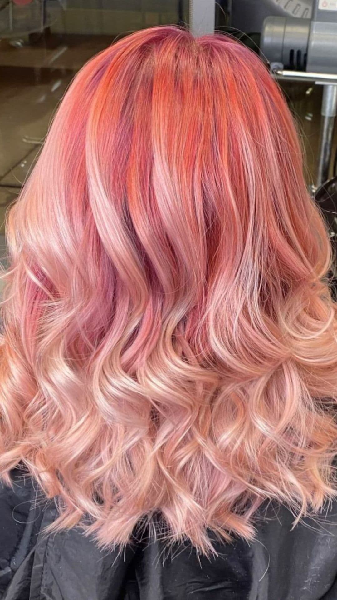 Back view of a person with a Peppermint Swirl hairstyle, featuring vibrant pink and orange tones in wavy layers.