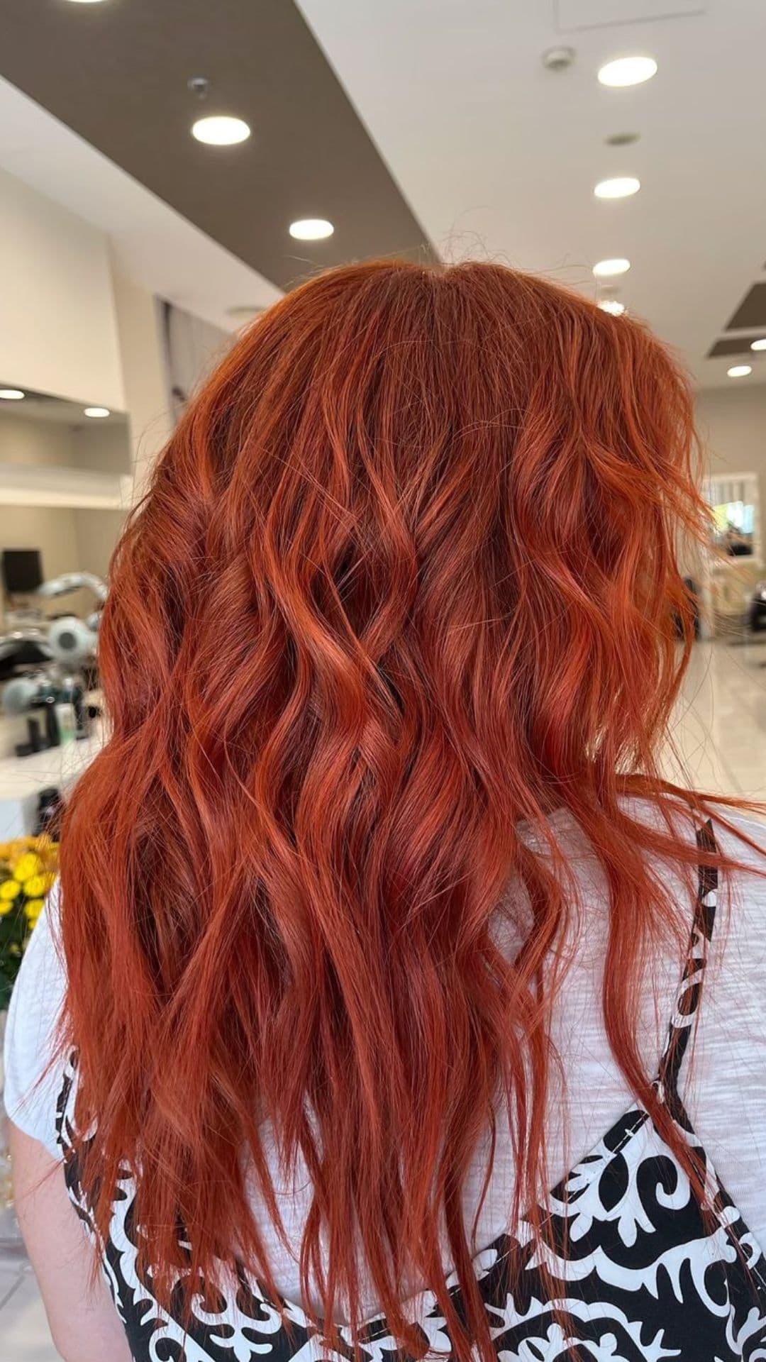 Person with long, wavy red velvet hairstyle, photographed from the back in a salon setting.