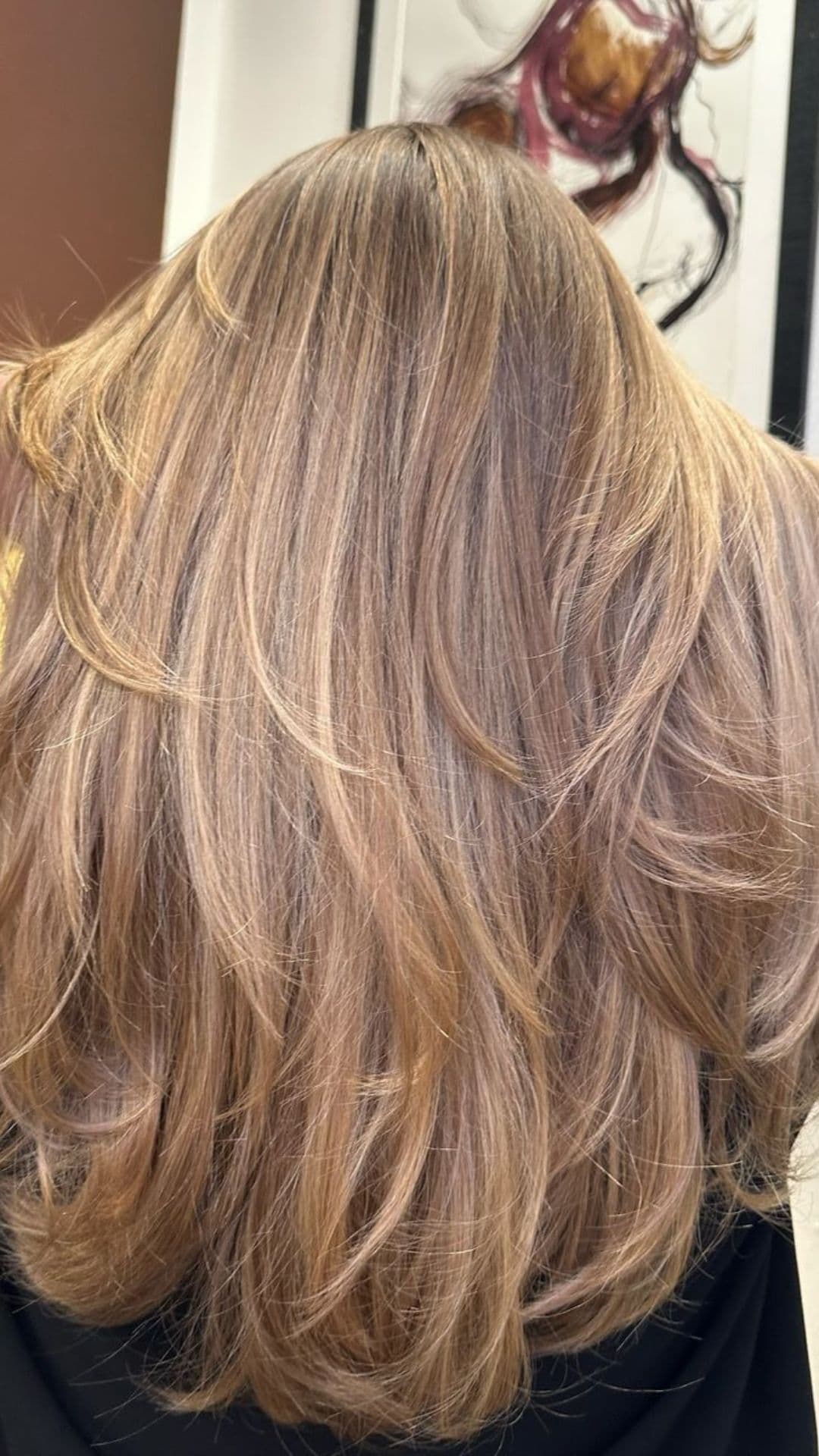 Woman showcasing a Caramel Balayage hairstyle from the back. Hair falls in soft layers, highlighting the caramel tones.