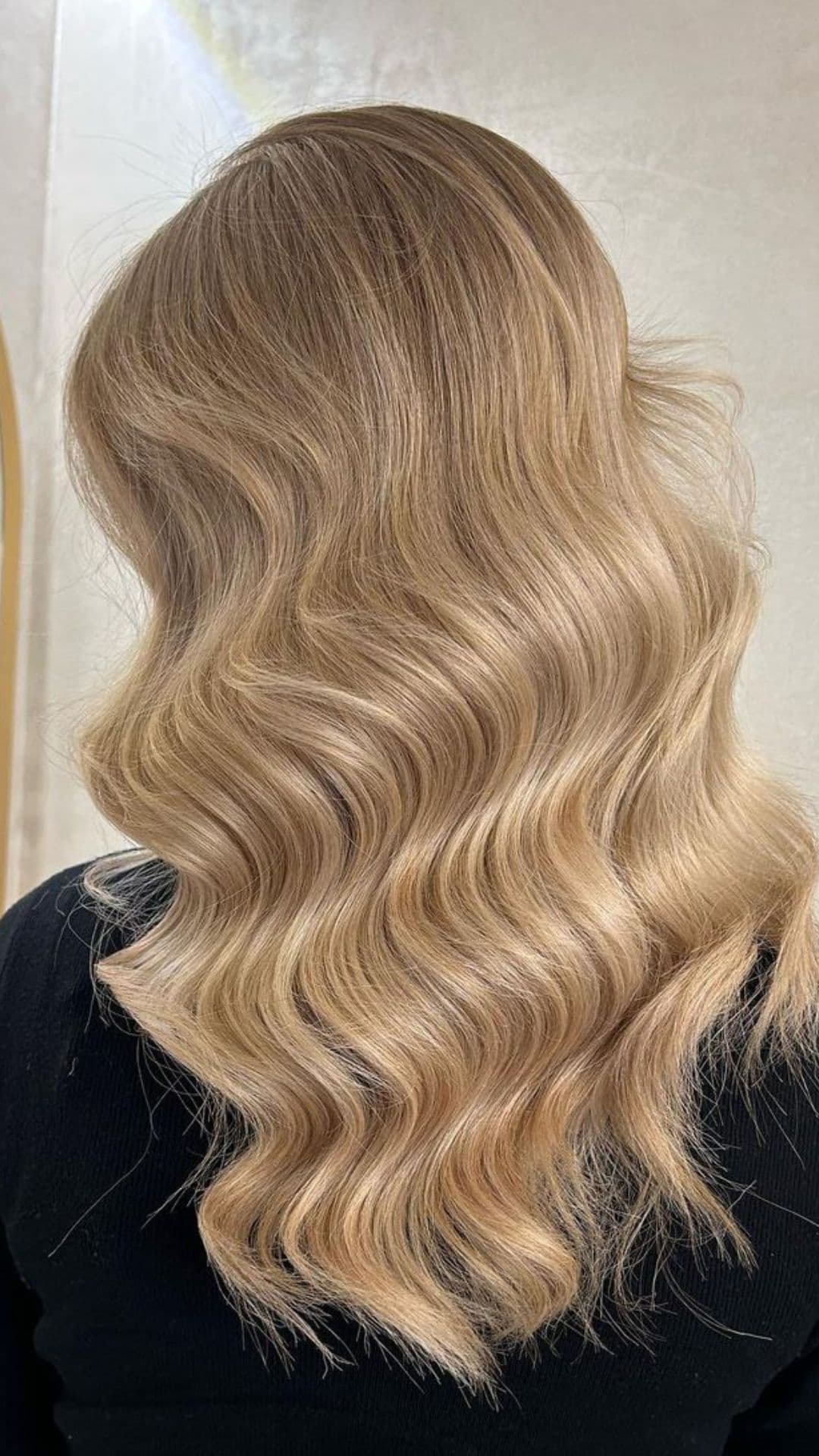 You see someone modeling a Dirty Blonde hairstyle. The hair is wavy, smooth, and reaches past the shoulders, with subtle highlights adding depth.