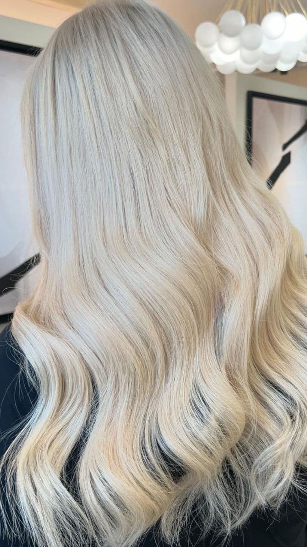 A person with long, wavy Icy Blonde hair is showcased from the back. The hair is smooth and shiny, reflecting light beautifully.