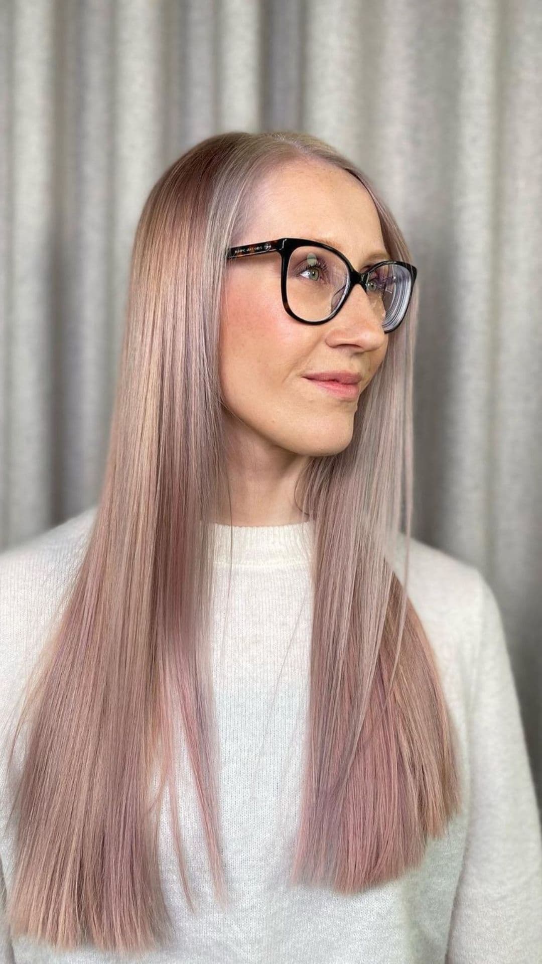 A person with long, straight, metallic pink hair wearing glasses and a white sweater.