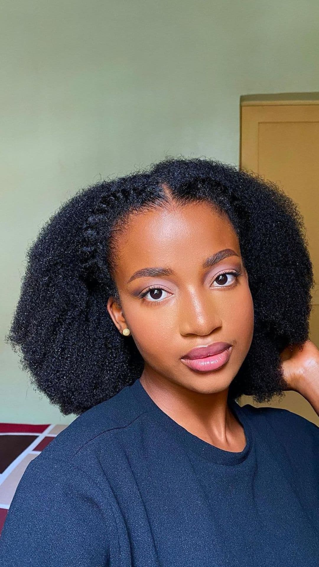 Person with Afro hairstyle wearing a black top, looking directly at the camera, with a calm expression.