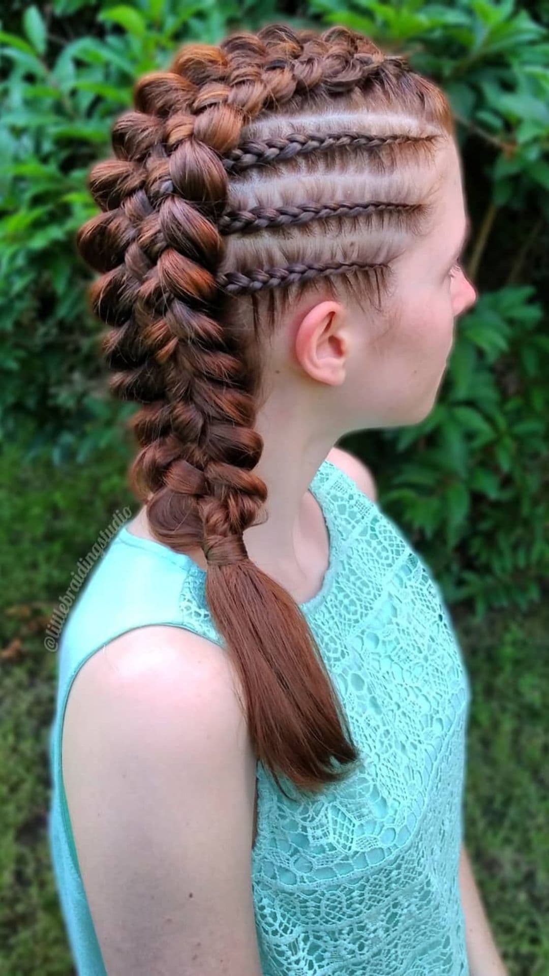 Person with a Five-Strand Dutch Ponytail hairstyle, wearing a light blue lace top, standing outdoors.