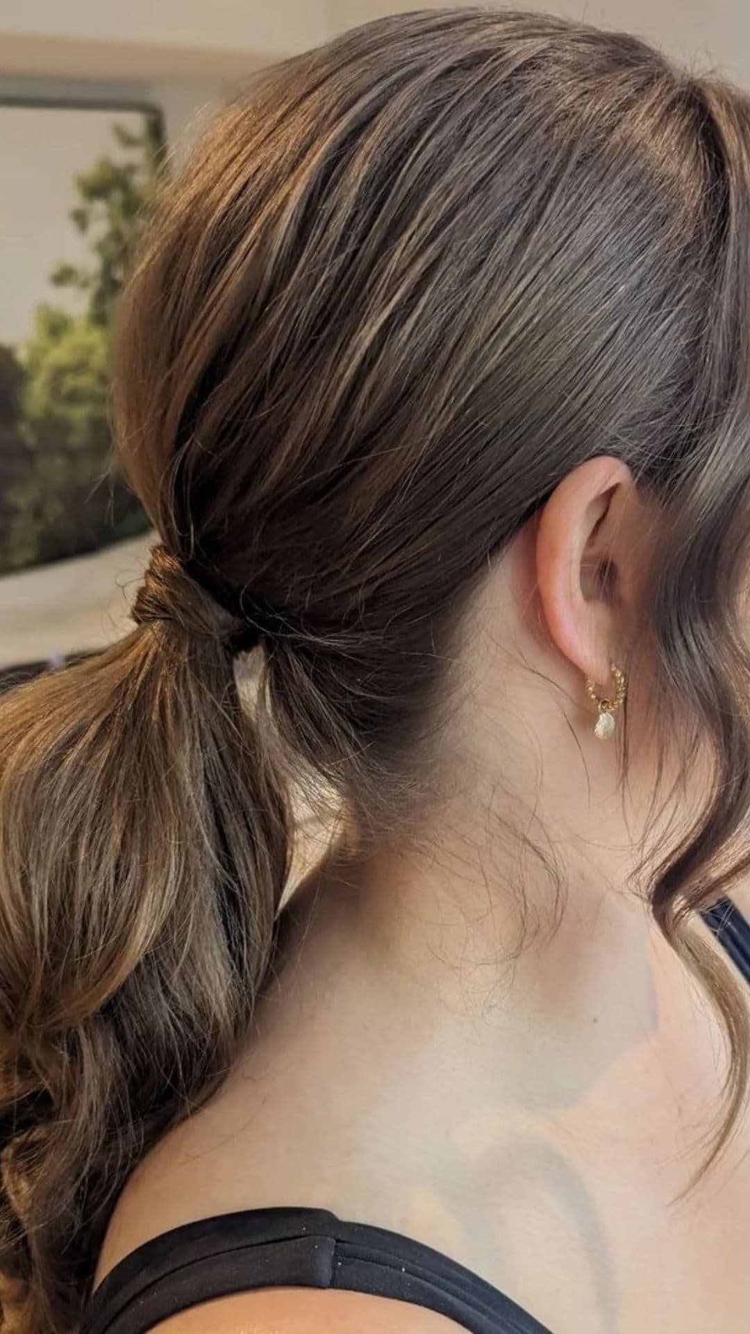 Side view of a person modeling a low textured ponytail hairstyle, showcasing the neat tie and smooth finish.