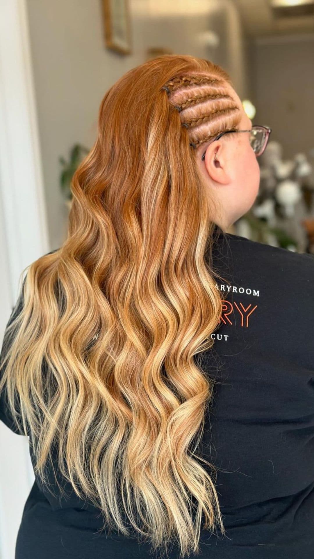 Woman with long, wavy hair styled in a side braid, wearing glasses and a black shirt.