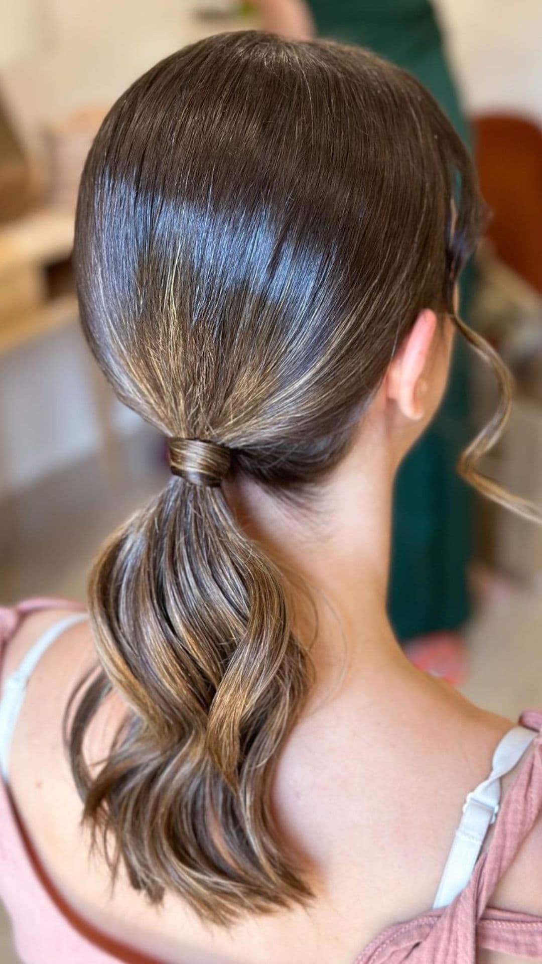 A person modeling a simple low ponytail hairstyle, with smooth, shiny brown hair.