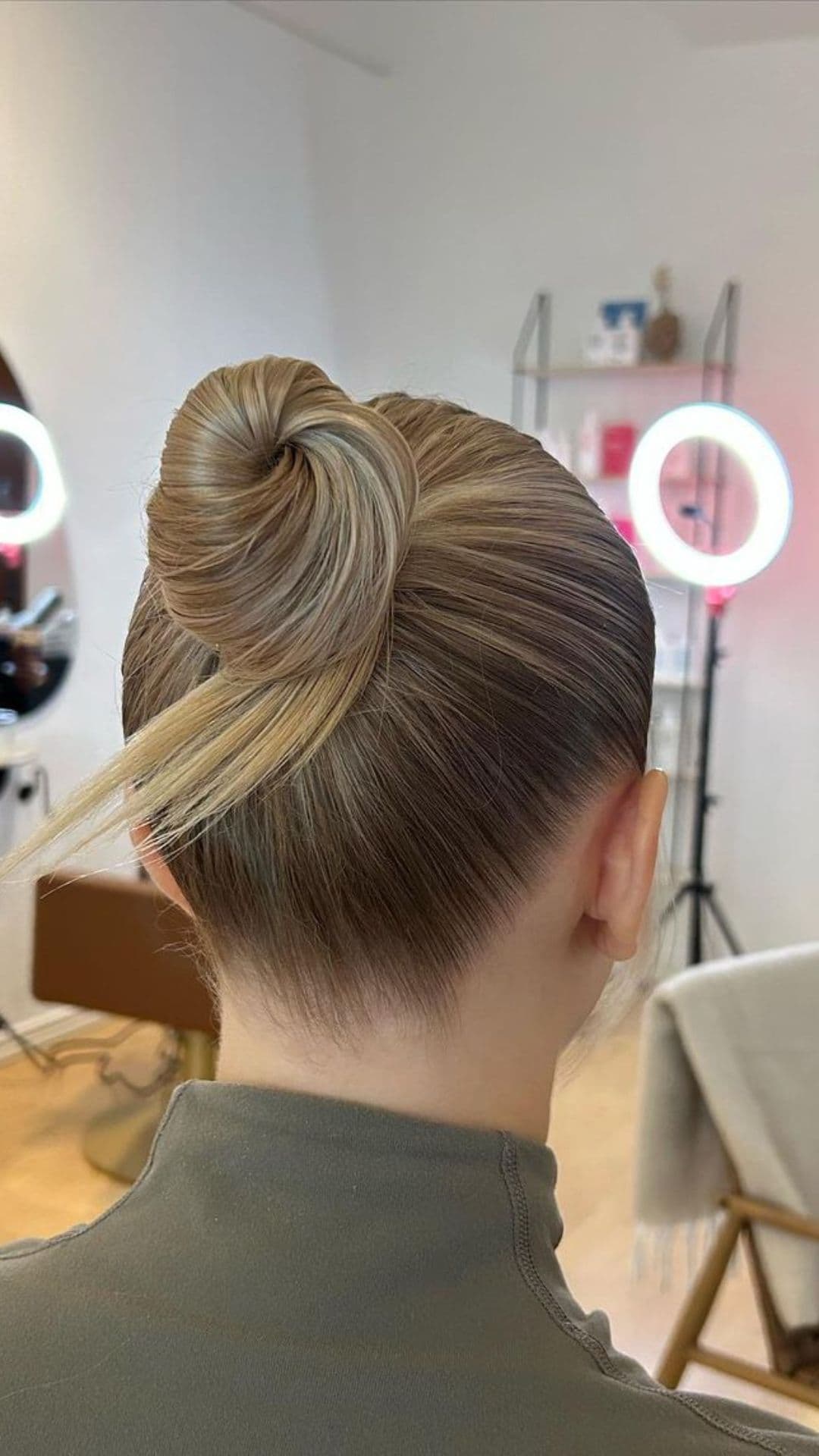 A person models a slick back bun hairstyle in a modern salon setting.