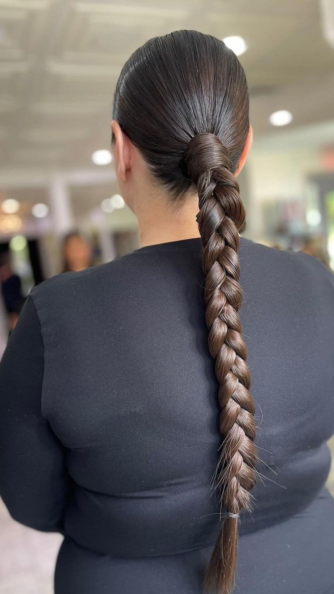 Woman with sleek braided ponytail hairstyle, shown from the back, wearing a black top.